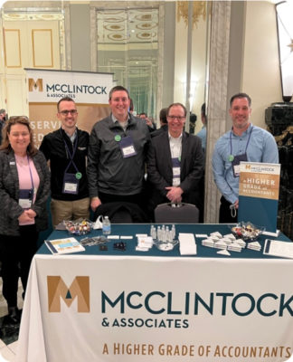 A group of McClintock team members standing behind their table at a conference.